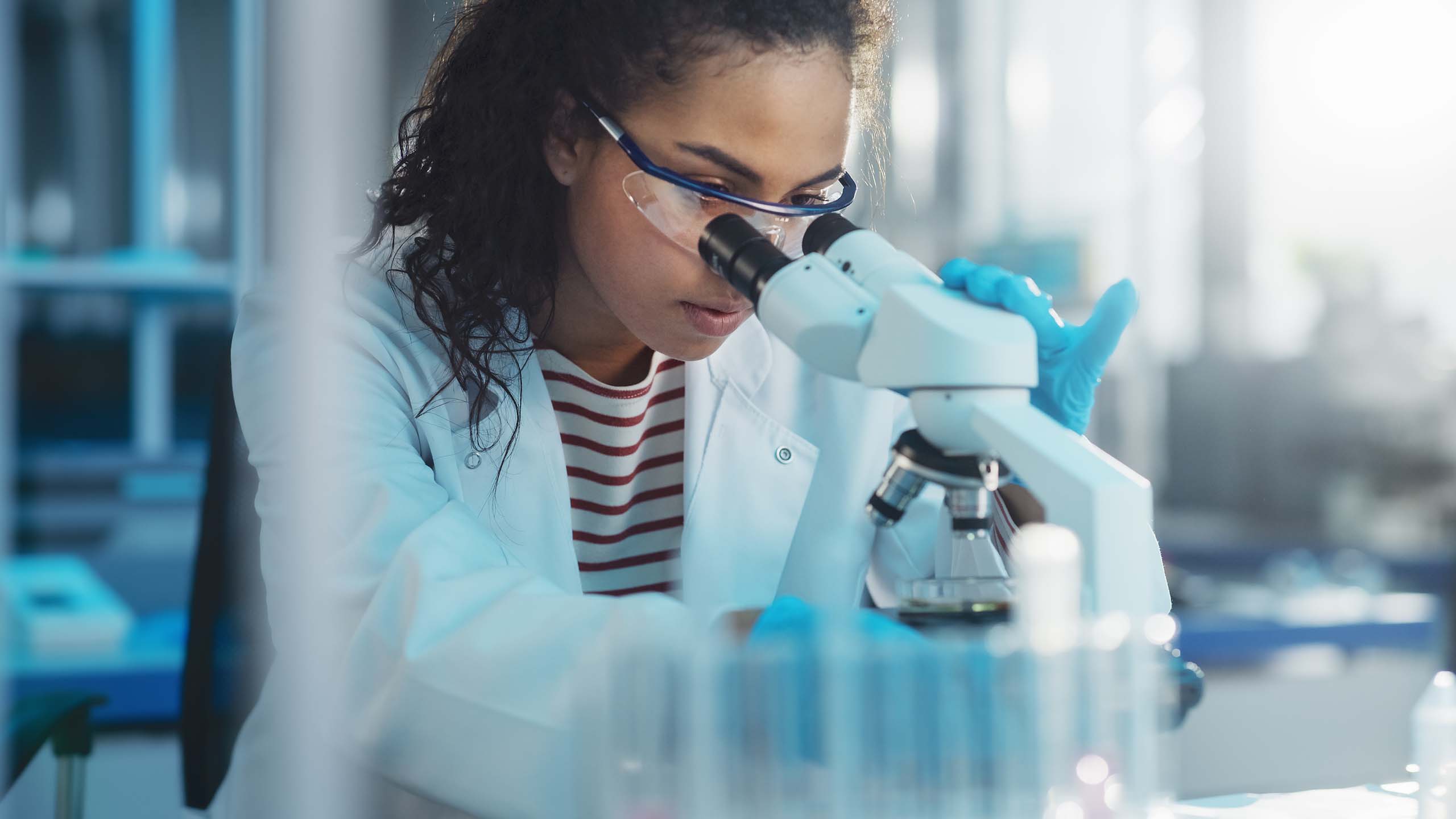 Young female diabetes researcher looks through a microscope in lab